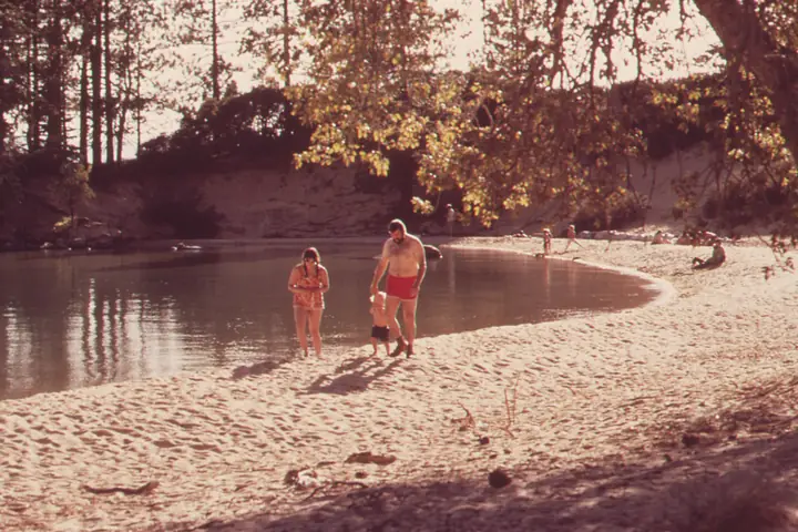 A family at the edge of a lake under pine trees