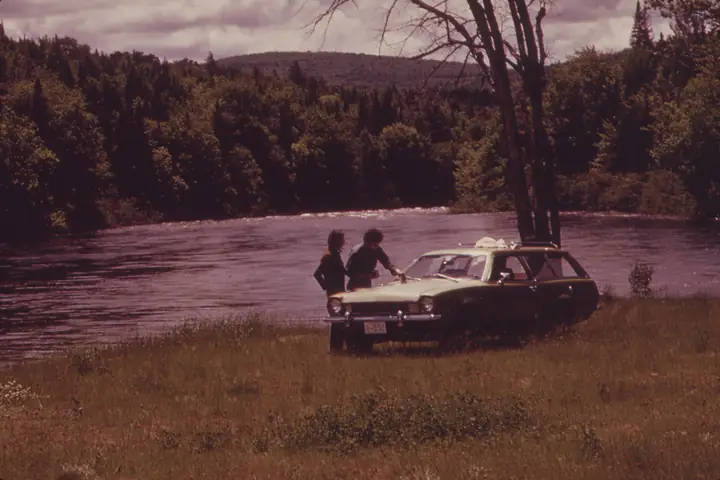 Campers waxing their car beside a river
